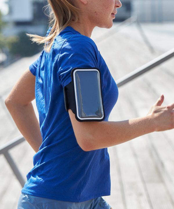 Una mujer corriendo al aire libre, llevando un brazalete deportivo magnético Shapeheart con funda desmontable, sujeto en su brazo.