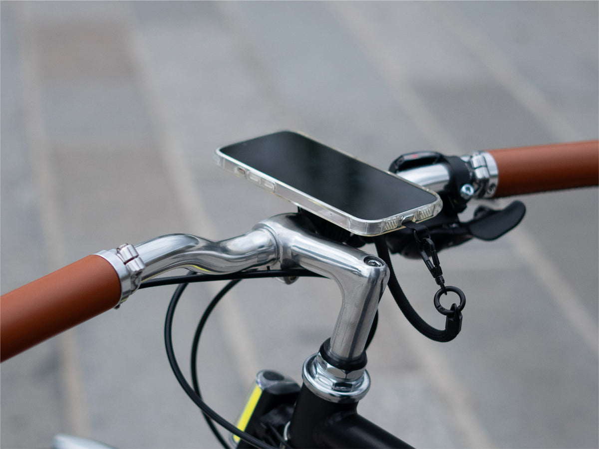 Smartphone fijado magnéticamente al soporte de manillar, demostrando una instalación minimalista. Uso del cordón para mayor seguridad.