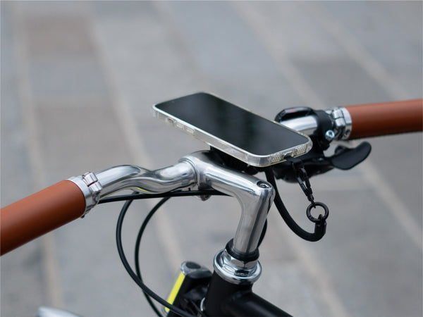 Smartphone fijado magnéticamente al soporte de manillar, demostrando una instalación minimalista. Uso del cordón para mayor seguridad.