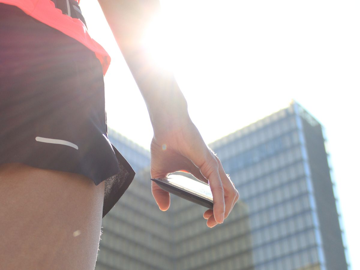 Corredora en ropa ligera corriendo al amanecer con un cinturón de running que contiene una pequeña botella, símbolo de la hidratación estival.