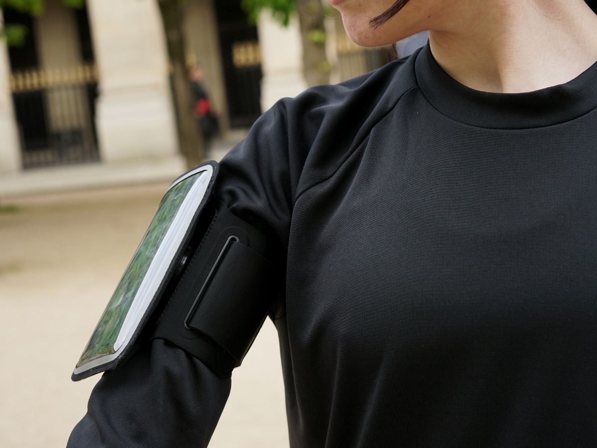 Corredor con chaqueta impermeable corriendo bajo la lluvia con un brazalete resistente al agua visible en el brazo, ilustrando la protección de los dispositivos electrónicos durante la carrera.