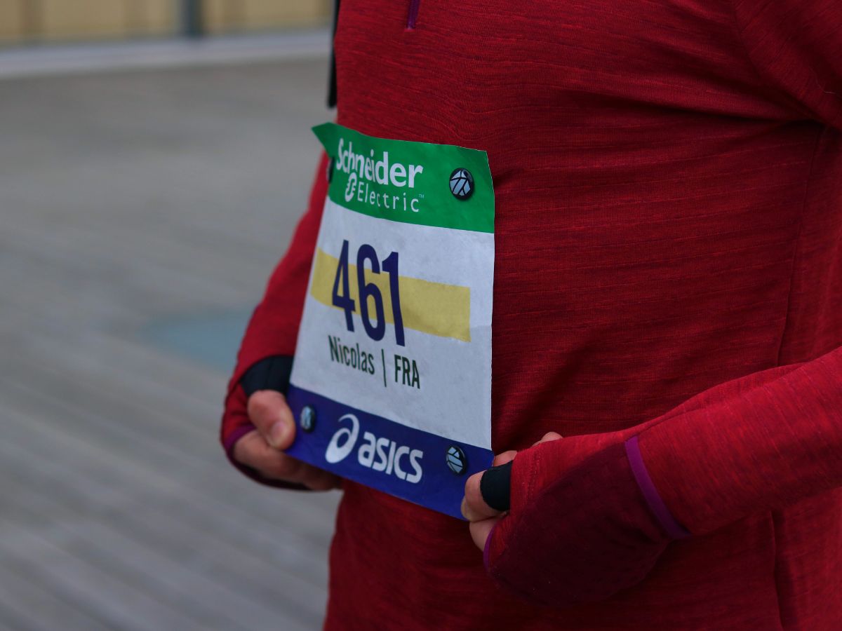 Atleta en la salida de una competición llevando un dorsal sujeto por imanes en una camiseta técnica, ilustrando la preparación óptima para una carrera oficial.
