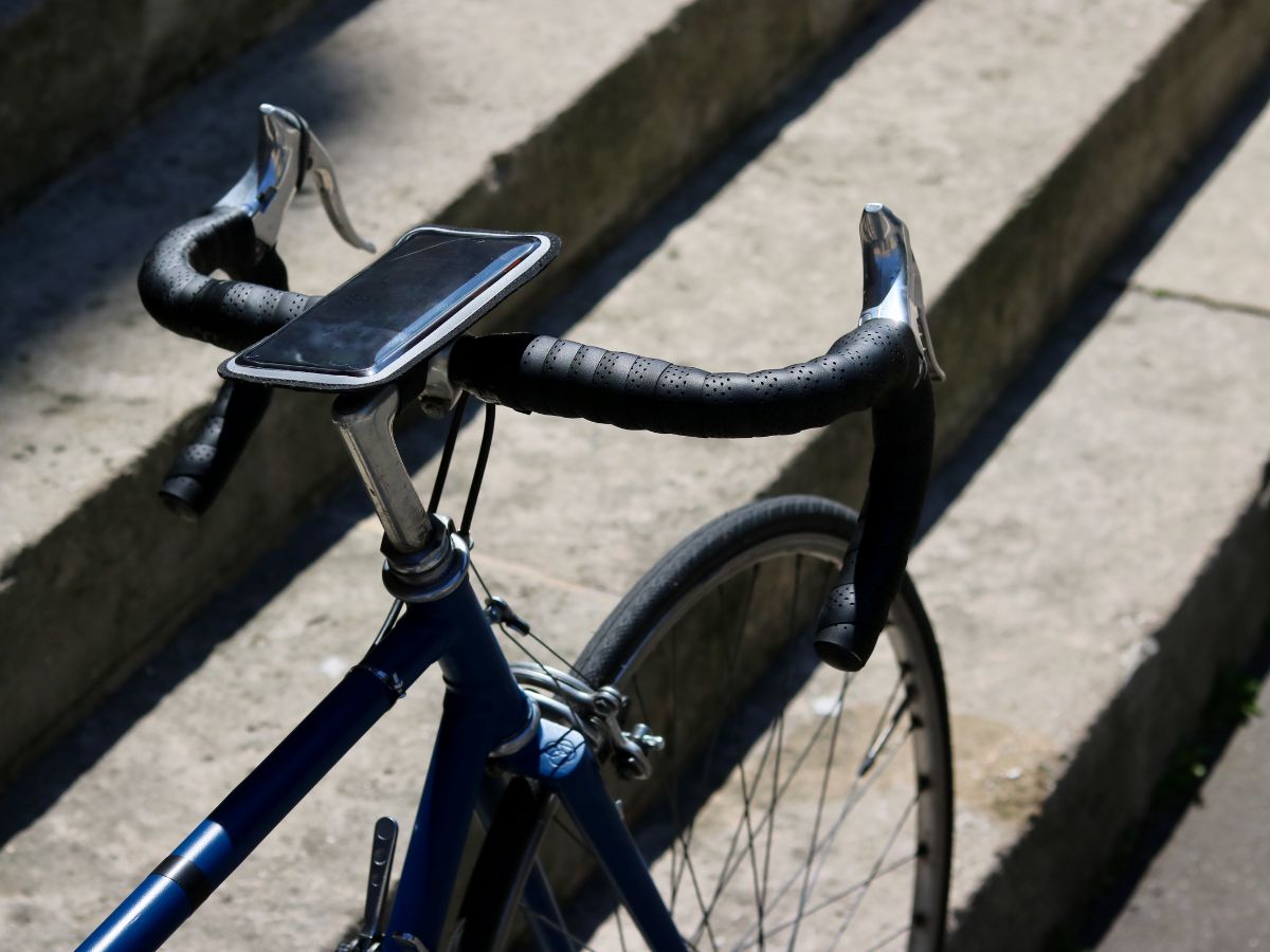 Soporte magnético para smartphone fijado en el manillar de una bicicleta de carretera, mostrando una aplicación GPS en acción.