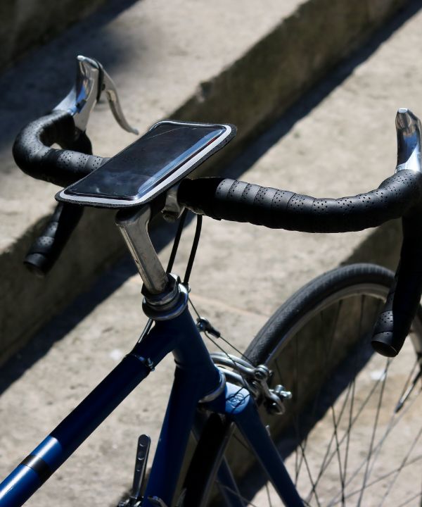 Soporte magnético para smartphone fijado en el manillar de una bicicleta de carretera, mostrando una aplicación GPS en acción.