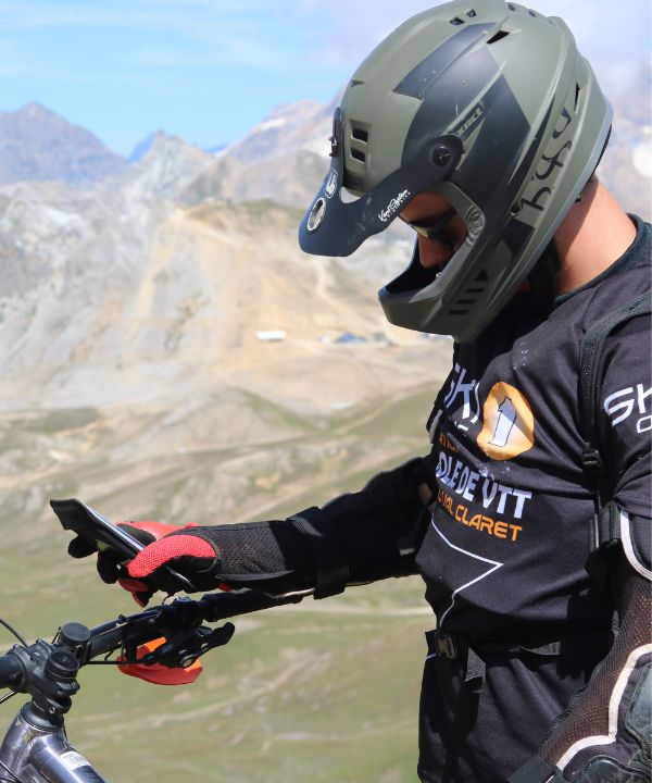 Primer plano de un soporte de bicicleta Shapeheart fijado al manillar de una bicicleta de montaña, smartphone visible, incluso en terreno accidentado.